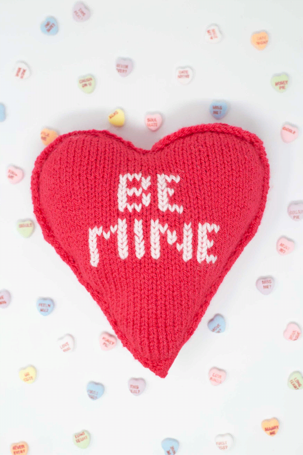 An animated gif showing 7 different pastel colored knit heart shapes with conversation heart saying embroidered on them