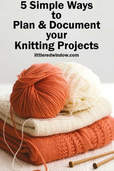 rust orange and white folded sweaters with matching balls of yarn on top and wood knitting needles below in front of a light gray background