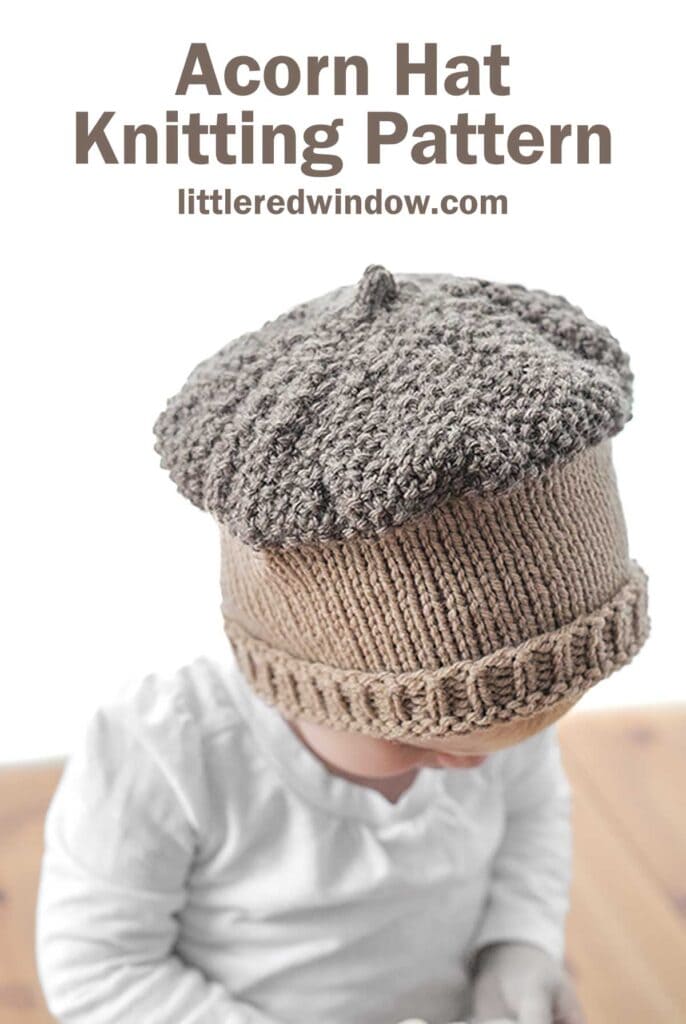 A baby wearing a knitted acorn hat and white shirt looks downward. The hat, with its textured top resembling an acorn cap, captures a rustic charm. Above, text reads: