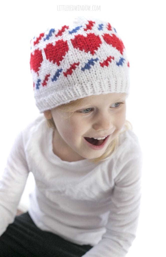 little girl laughing and wearing a white knit hat with red hearts and blue and red airmail stripes
