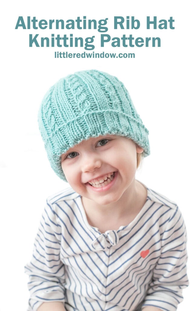 smiling girl in teal knit hat with alternating ribs of plain and cabled stitches and a folded up brim