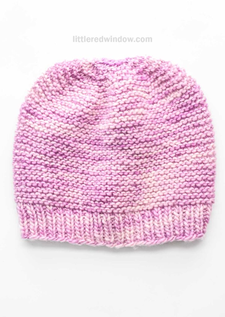 A hand-knitted garter stitch hat in shades of pink and white with a textured pattern, displayed on a white background.