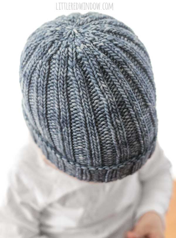 Top view showing the ribbing decreases of child wearing medium denim blue knit easy ribbed hat knitting pattern with 2x2 ribbing and folded up brim in front of a white background