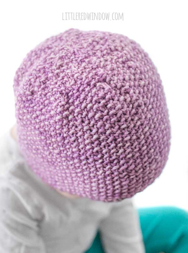 closeup showing the top of the lavender purple knit seed stitch baby hat knitting pattern on a toddler in a white shirt