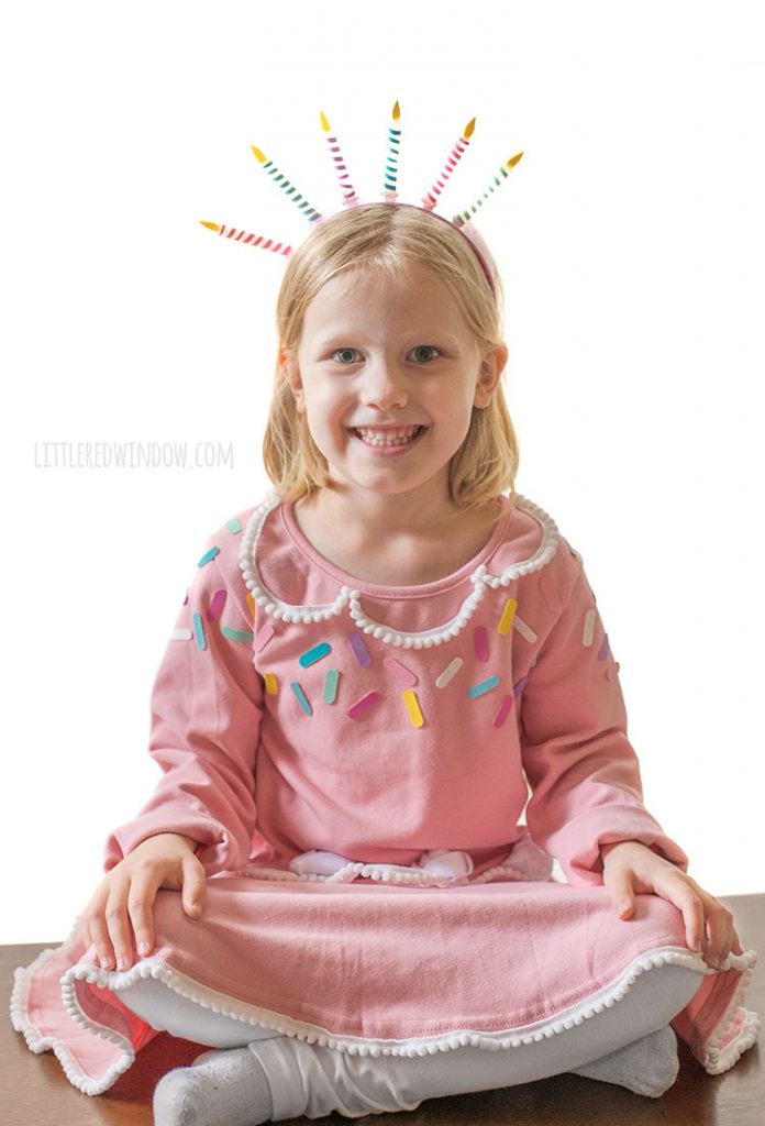 girl casually sitting on a table wearing a pink birthday cake costume with a candle headband