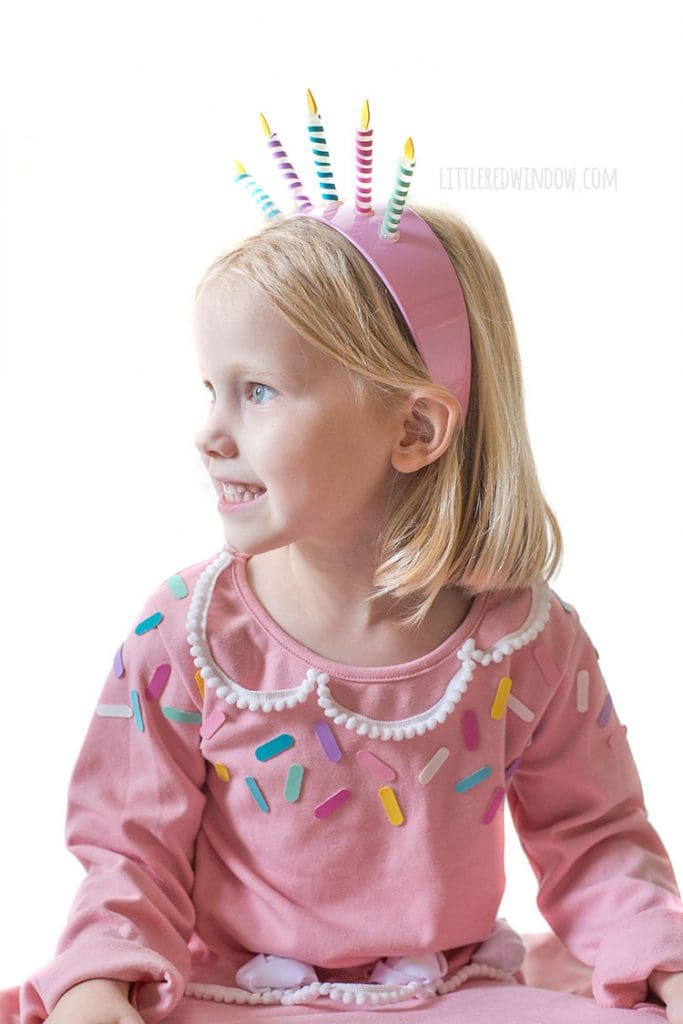 closeup of girl in pink birthday cake costume with birthday candle headband smiling and looking off to the left