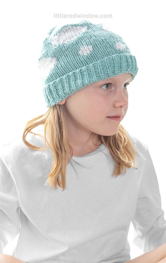 child wearing blue sky hat knitting pattern blue hat with white clouds on it looking slightly to the right