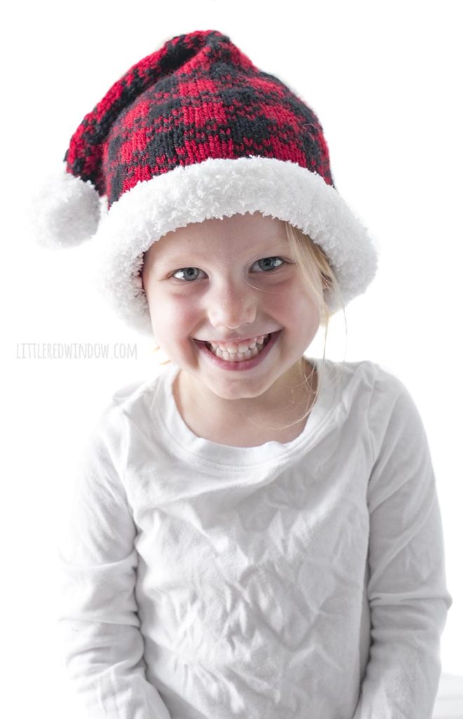 smiling girl wearing red and black plaid santa hat and white shirt