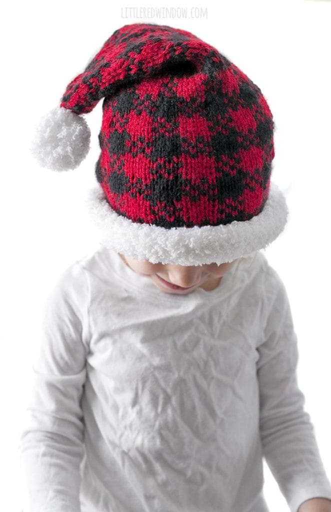 little girl looking down and wearing a red and black buffalo plaid santa hat