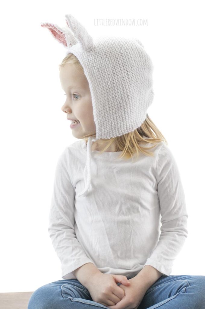little girl wearing white knit bonnet with bunny ears and looking off to the left