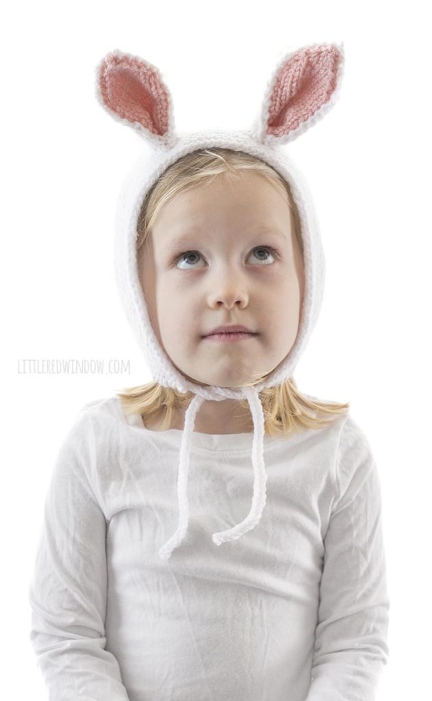 little girl wearing white knit bonnet with bunny ears and looking up at the ceiling