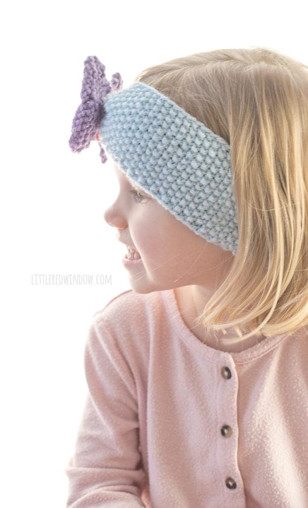 side view of little girl in pink shirt wearing blue knit headband with purple butterfly on the front
