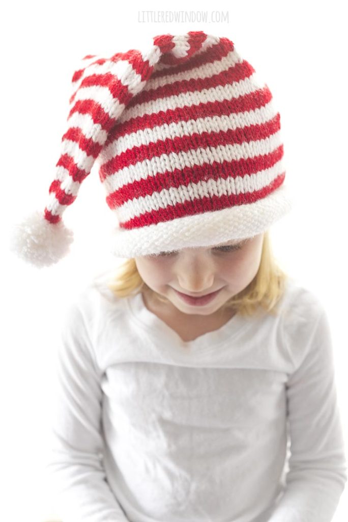 girl in white shirt looking down at her lap and wearing a red and white striped knit stocking cap with white rolled brim and white pom pom