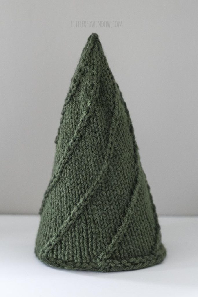 The Medium Cozy Christmas tree is knit in dark green worsted weight yarn with simple lines of twisted stitches.