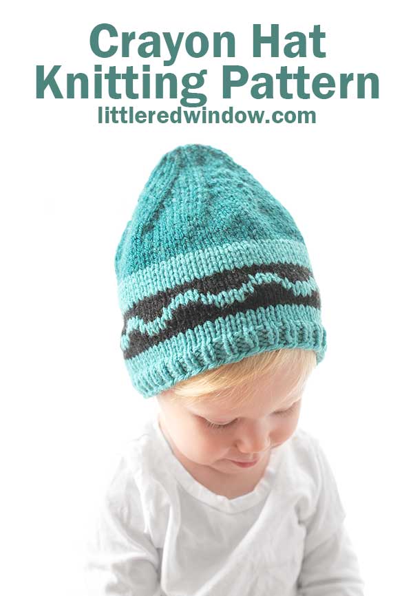 girl in white shirt wearing a teal knit hat with pointed top and black wave design that looks like a crayon looking down at their lap