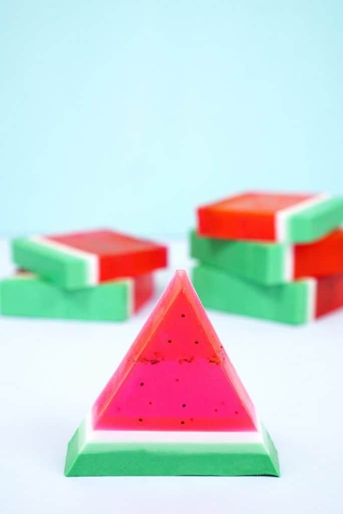 Triangle wedge of green white and red watermelon soap with more soap stacked in the background.