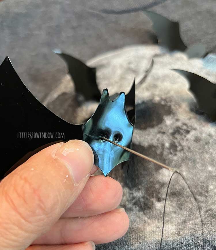 hand using needle to punch two small holes in the plastic bat shape