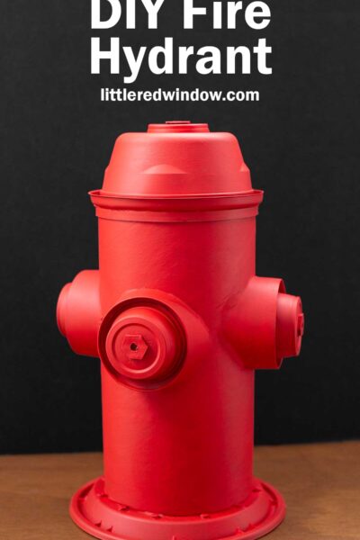 A red DIY fire hydrant made from recycled materials, set against a black background. The text above reads "DIY Fire Hydrant" with a website link "littleredwindow.com.