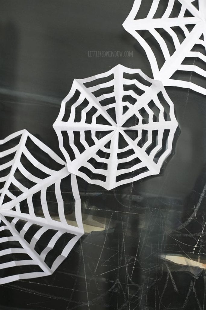 Closeup of three paper spiderwebs strung together on a wall