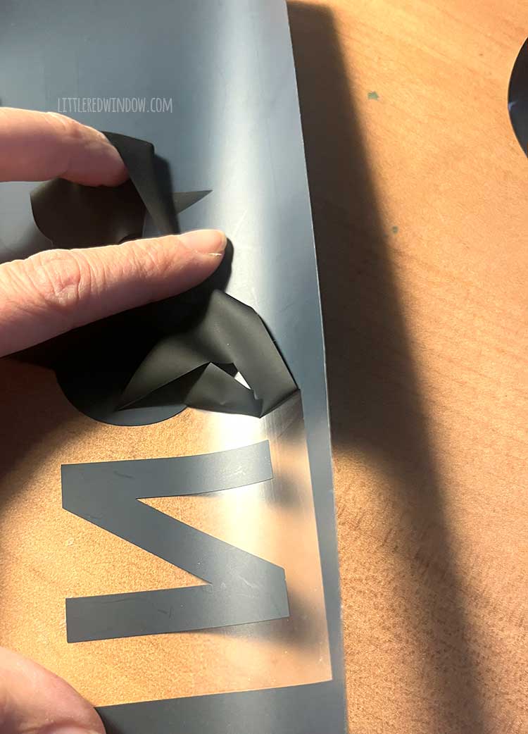 a hand weeding black heat transfer vinyl on top of a wood desk top