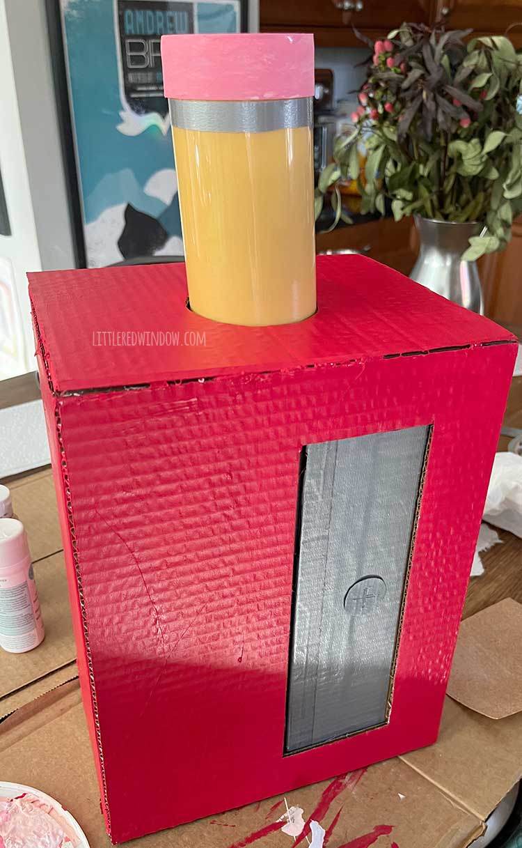 finished red cardboard box pencil sharpener with large faux pencil sticking out of the top on a wood kitchen island