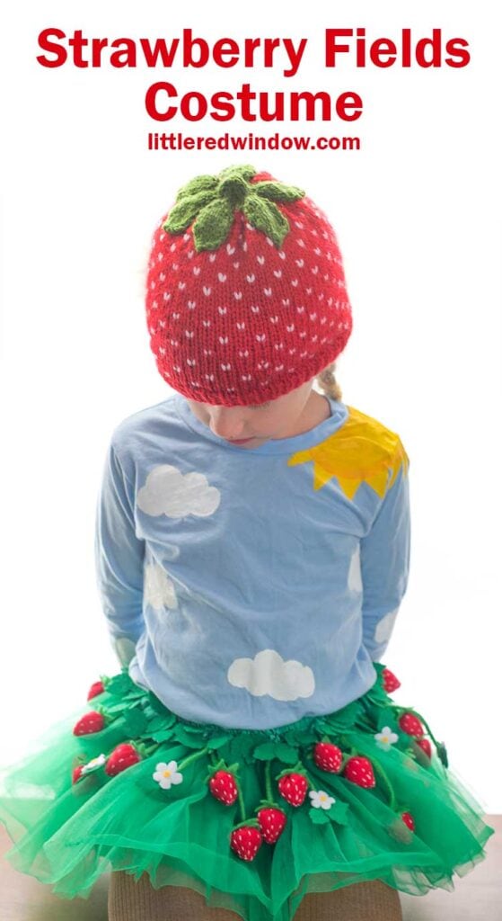 girl wearing a strawberry hat and green tutu skirt with felt strawberries all over it looking down at her lap