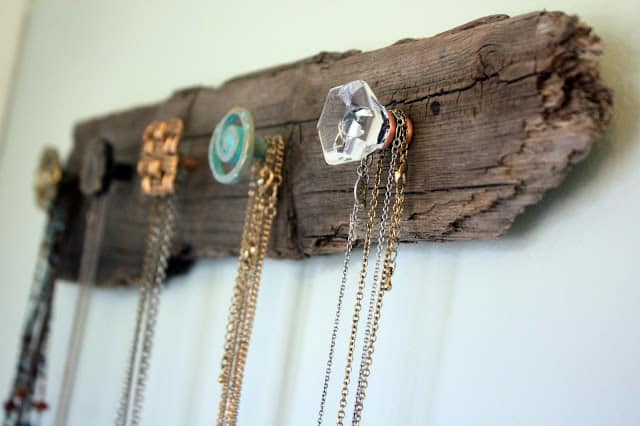 A piece of driftwood on the wall with decorative knobs added to hold necklaces