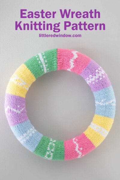 Colorful knitted Easter wreath with sections in pastel shades of green, pink, purple, blue, and yellow, each with white patterns. Text at the top reads "Easter Wreath Knitting Pattern littleredwindow.com.