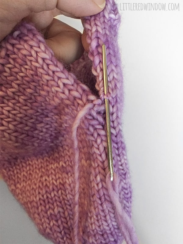 Hand holding the hat and using a yarn needle to demonstrate the Easy Knit Flat Baby Hat Seam technique