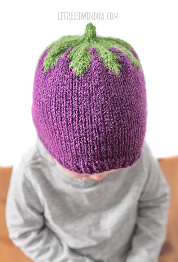 view from slightly above of baby wearing purple and green knit eggplant hat