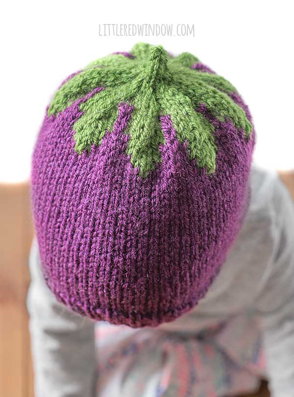 view from slightly above and to the left of baby wearing purple and green knit eggplant hat