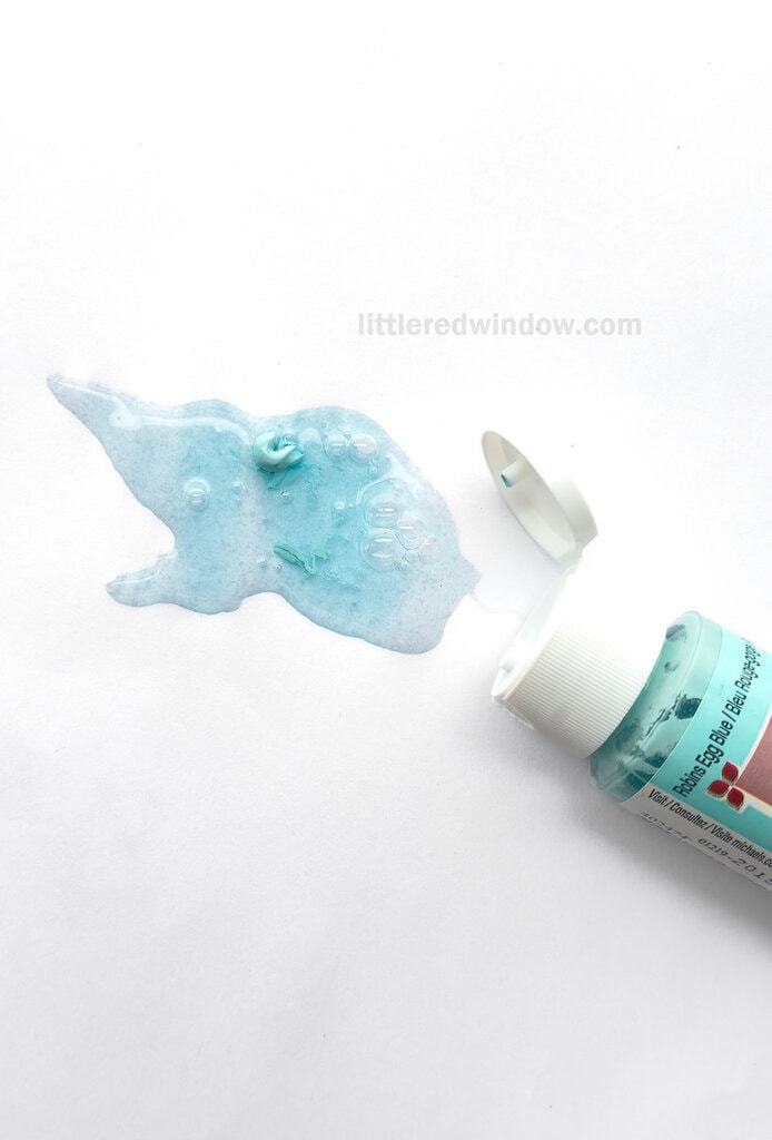 bottle of blue craft paint open next to a puddle of expired separated paint