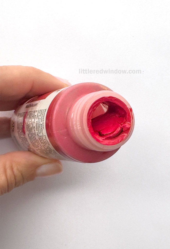 hand holding an open bottle of red acrylic craft paint showing that the paint inside has dried out