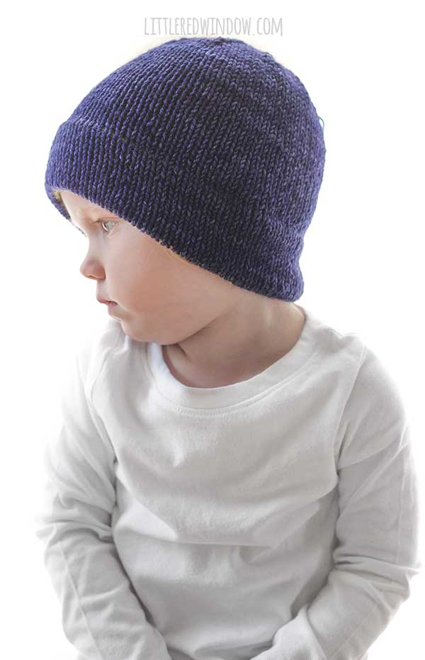 child in white shirt wearing a navy blue knit hat and looking off to the left