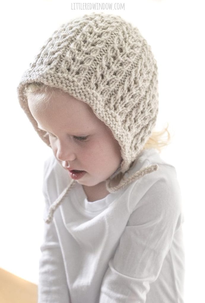 toddler girl wearing tan lace bonnet and looking down