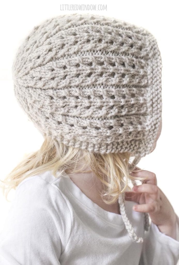 This easy ribbed lace knitting stitch makes the Flutter Lace Baby Bonnet knitting pattern so special and unique picture of a girl wearing bonnet looking off to the right