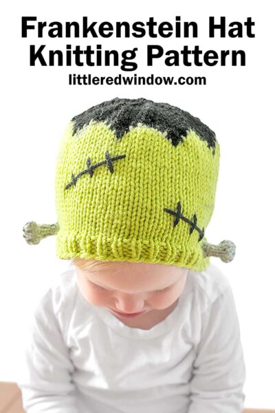 A baby wearing a green knitted Frankenstein Hat designed to resemble Frankenstein's monster, with black hair-like detail at the top and stitched patterns on the sides. The hat has small protrusions on each side, mimicking bolts. The text at the top reads, "Frankenstein Hat Knitting Pattern.