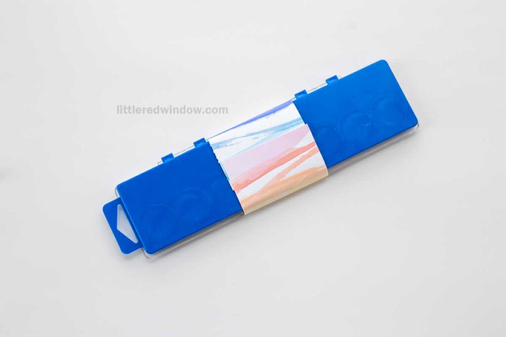 A rectangular blue watercolor paint set with a colorful pastel cardboard sleeve lies closed on a white background.