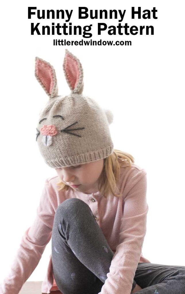 little girl in pink shirt looking down at the ground and wearing a tan knit bunny hat with ears and a tail
