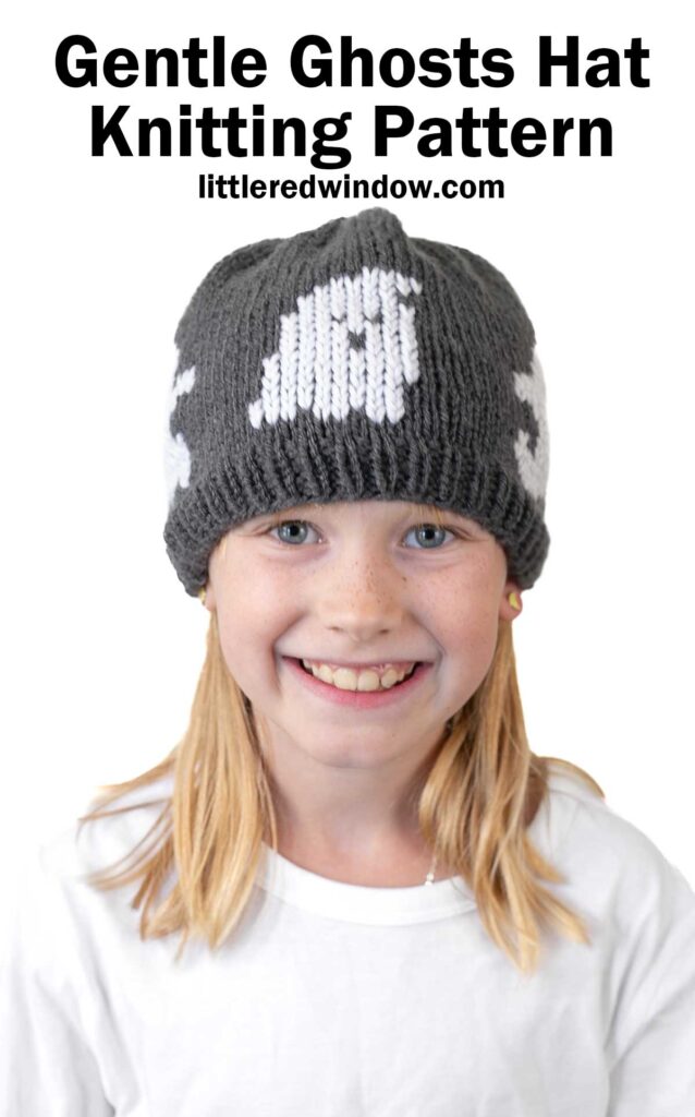 Cute girl wearing a gray knitted ghost hat with white pumpkin design for fall or Halloween.