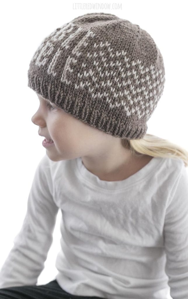 side view of girl wearing brown knit hat with gobble gobble pattern on front and zig zag pattern around the sides