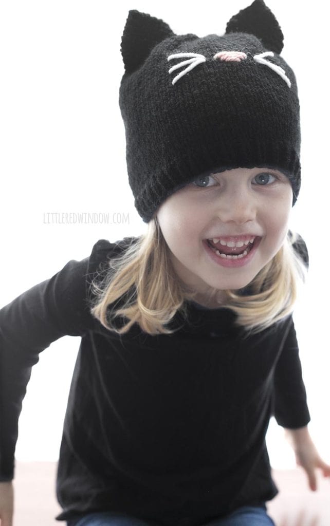 little girl laughing wearing a black shirt and knit black cat hat