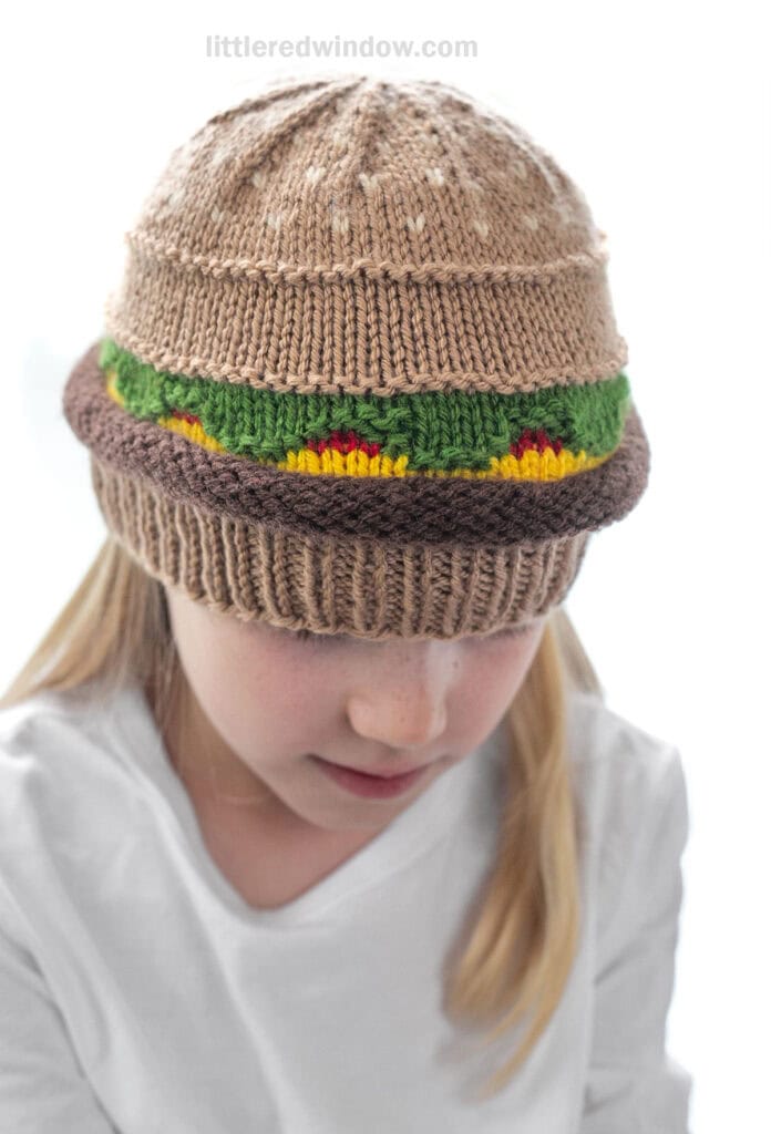 Closeup of child wearing knit hamburger hats showing the sesame seed pattern on top of the bun slash hat