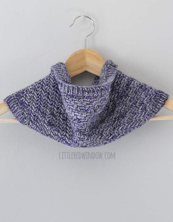 front view of purple knit cowl hanging on a light wood hanger in front of a light gray wall