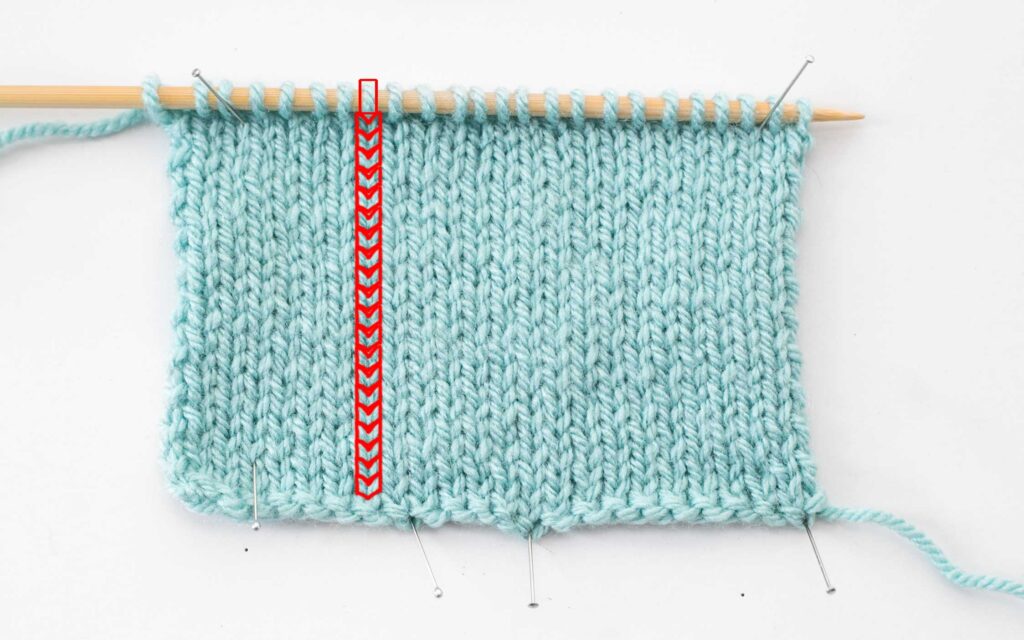 an unfinished stockinette stitch sample with the individual stitches in one column outlined in red