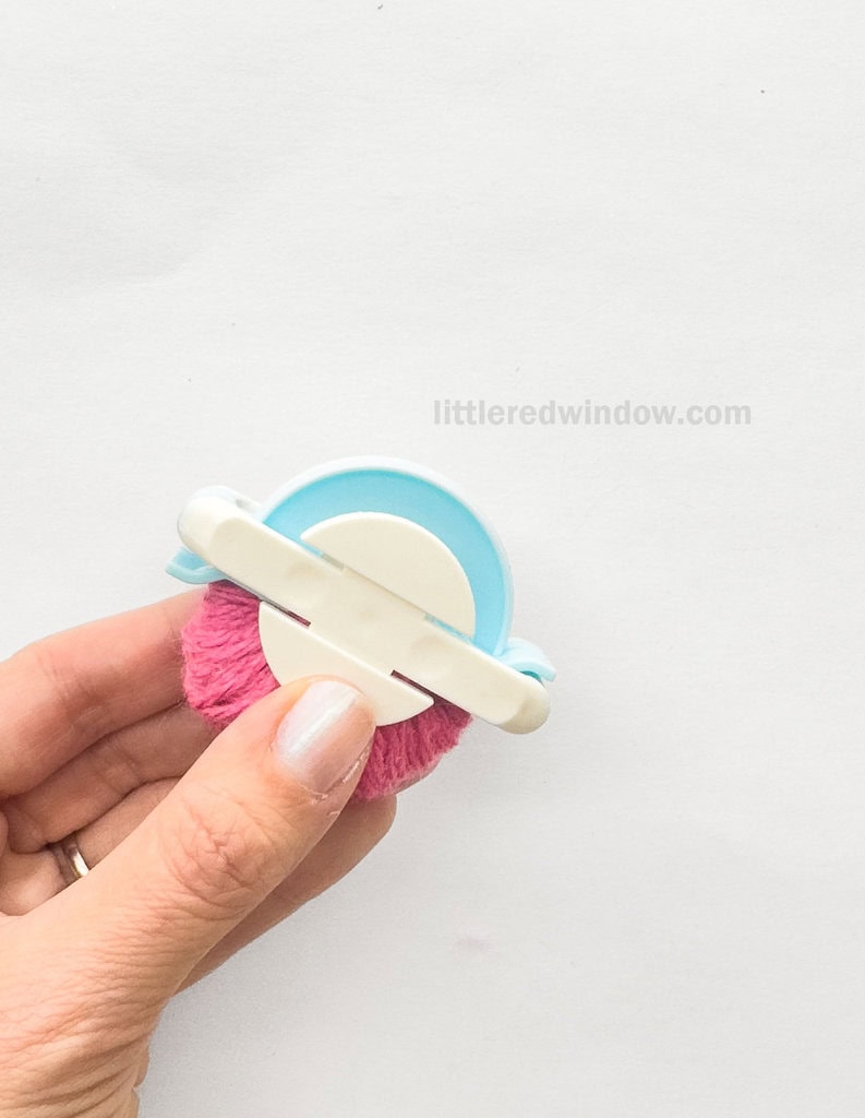 your pom pom maker, it is made up of a central circular part connected with a peg in the middle and two sets of arch pieces on either side of the circle that open and close.