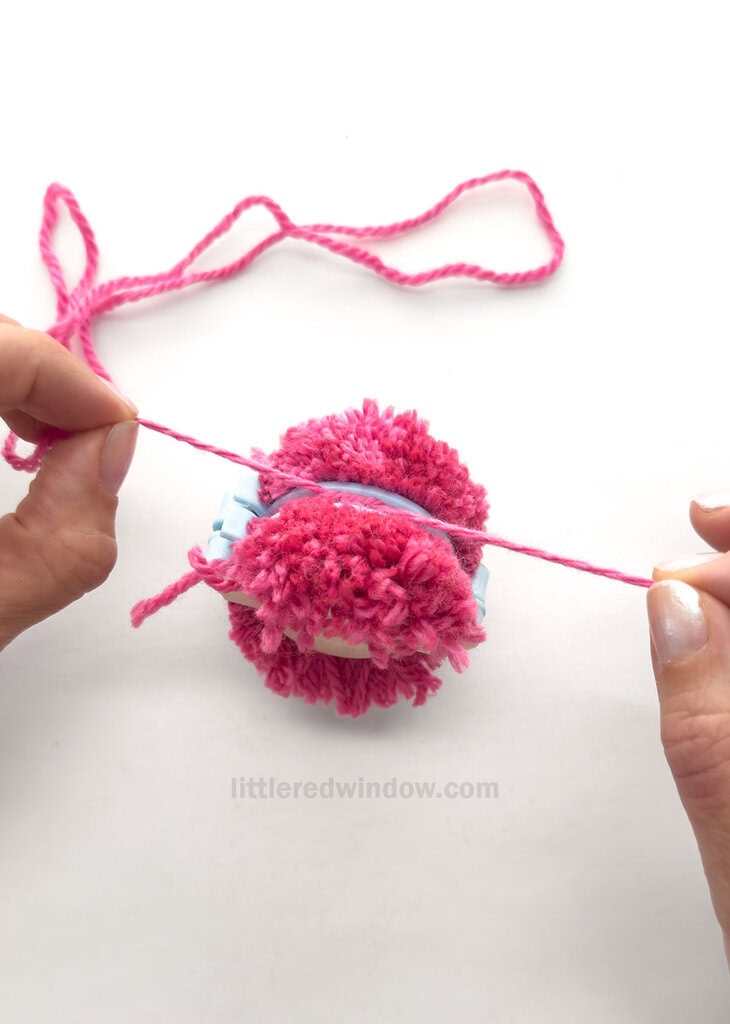 Using the piece of yarn you set aside at the beginning, wrap it around the circumference of the pom pom maker in the gap between the arches where you just cut. Pull as tightly as you can and double knot.