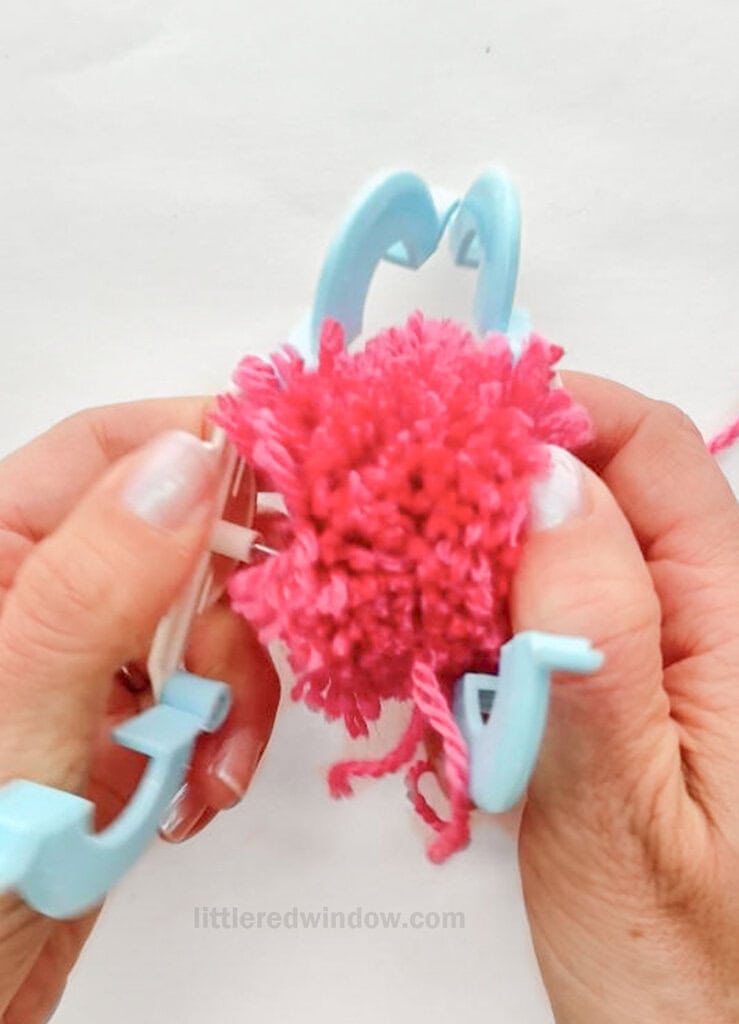 When the arches are open, separate by the two halves of the pom pom maker that are still connected at the center of the circles, by pulling them apart gently. This will release the entire pom pom from the pom pom maker.