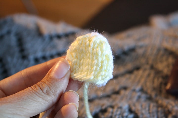 hand holding a light yellow knit bear ear in front of a dark background