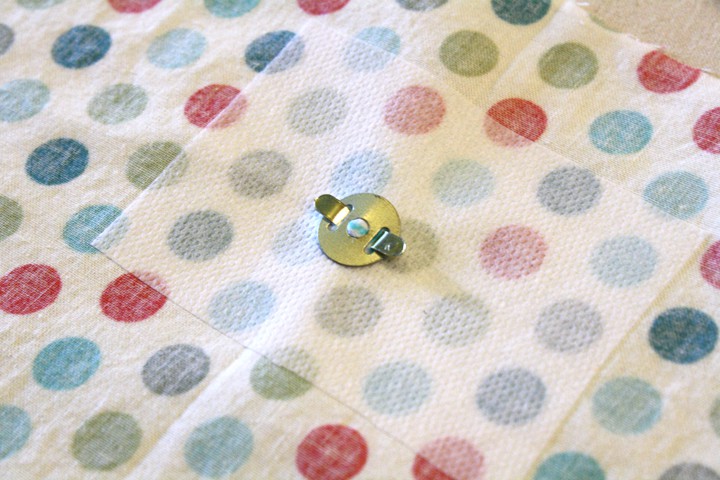 the back side of a metal snap with the tabs folded down to secure it